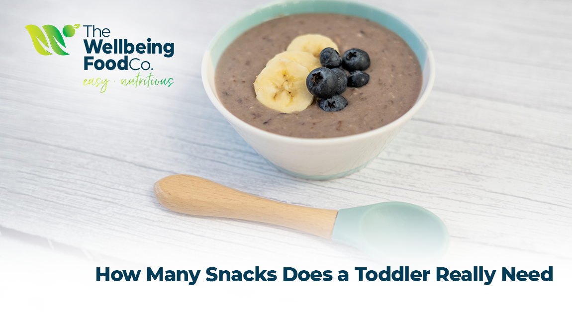 Smiling toddler eating healthy snack at a small table with fruit and whole grains.