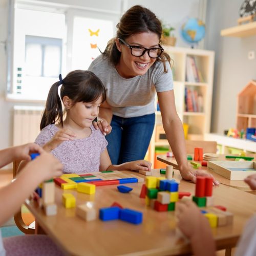 Preschool teacher with children playing with didactic toys Preschool teacher with children playing with colorful wooden didactic toys at kindergarten